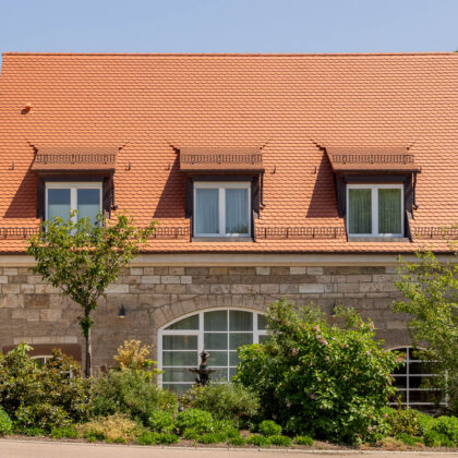 Landhotel mit Biberschwanzziegel Segmentschnitt in naturrot im Fokus das Nebengebäude.