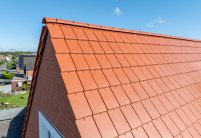 Naturrote Flach-Dachziegel auf Mehrfamilienhaus mit Klinkergiebel und Zubehör Ortgang im Fokus