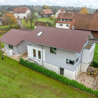 Rückansicht von Wohnhaus Dachziegel Z10 von Jacobi auf Baustilhaus in der Oberfläche edelweinrot mit schmuckvollem Firstanfänger der Serie F6v und Nebengebäude mit dem gleichen Ziegelmodell