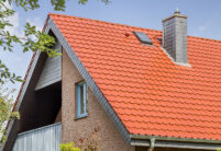 Giebelseite eines Klinkerhauses mit überdachtem Balkon. Auf dem Steildach unsere Flachdachpfanne J11v in edelkupfer.