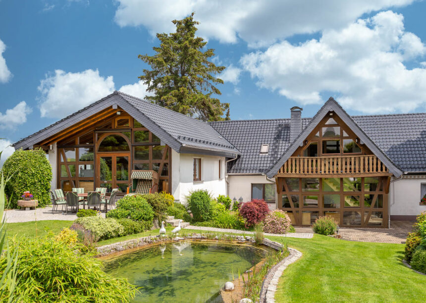Gesamtansicht von Einfamilienhaus mit Satteldach samt Gauben, gedeckt mit Allrounder J11v in sapcegrau, im Bild außerdem Gartenteich