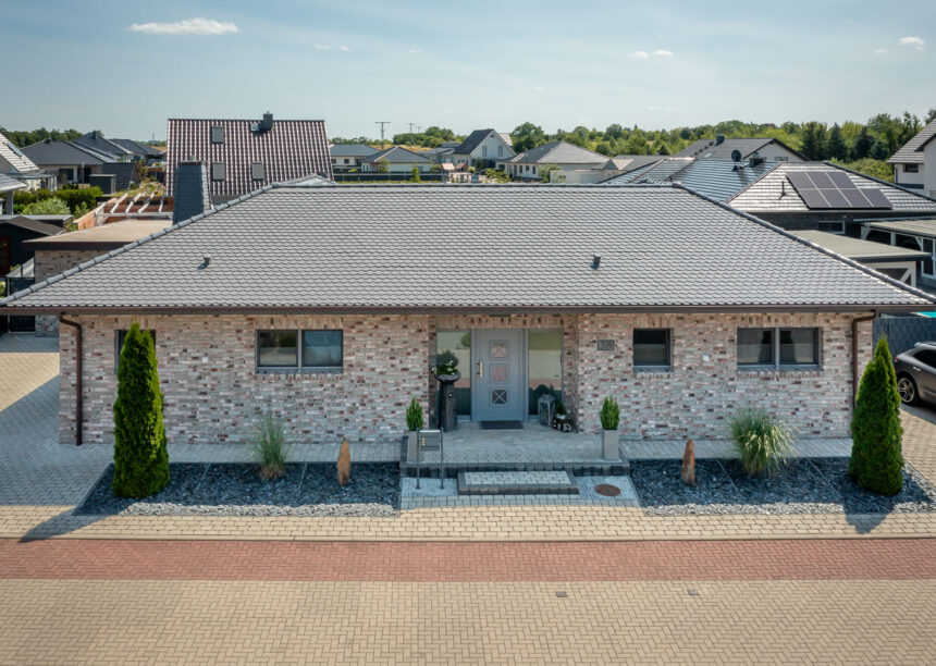 Sueddeutscher Biber Rundschnitt in silbergrau auf Walmdach-Bungalow mit Klinkerfassade.