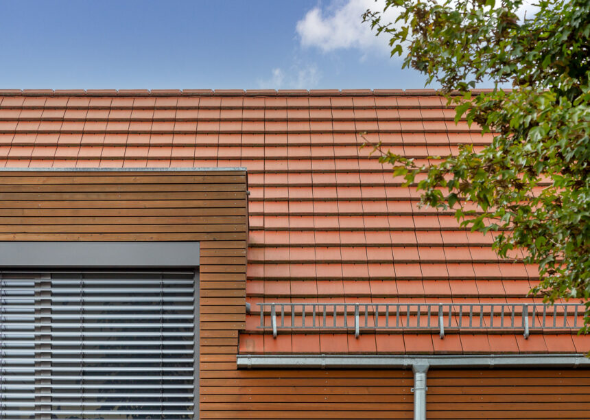 Flachziegel WALTHER Stylist® mit Dachziegeldetails in rotbraun auf Satteldach mit formschöner Gaube auf modernem Haus mit Holzverkleidung