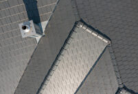 Ungewöhnliche Dachform trifft auf Flachziegel in edelschiefer auf der Vogelperspektive fotografiert mit Fokus auf den First und Walmkappe.