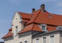 Tradition in rotbraun auf Mehrfamileinhaus mitten in der Stadt - der Dachziegel von Jacobi im Doppelmuldendesign. Im Bildfokus der das Walmdach mit Fußwalm