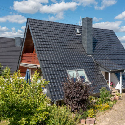 Dachhaus mit edelschwarzen Reformziegeln Z10. Hier der Eingangsbereich und überdachter Holzbalkon am Giebel.