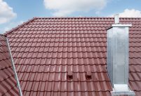 W6v in edelrosso auf L-förmigen Satteldach, der beliebte Dachziegel für Süddeutschland und Österreich hier mit Dachkehle und Sanilüfter im Fokus