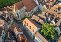Dach mitten in der Stadt mit Jacobi Biber Rundschnitt in naturrot schräg mit Kirche aus der Vogelperspektive