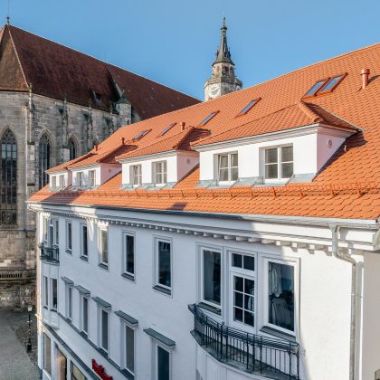 Dach mitten in der Stadt mit Jacobi Biber Rundschnitt in naturrot schräg mit Kirche im Hintergrund