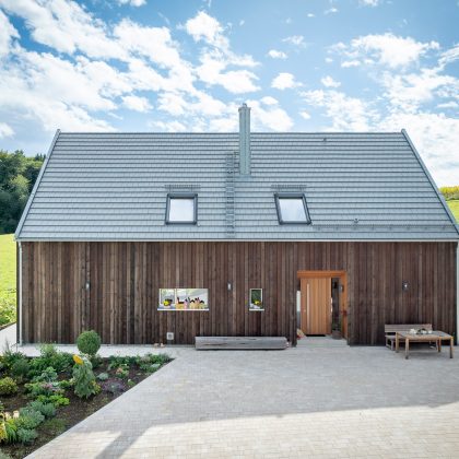 Dachziegel Stylist in edelgrau auf Holzvertäfelten Einfamilienhaus mit hochwertigem Jacobi Zubehör, Schneefanggitter, Sanitärlüfter und PV Solarträger Referenzobjekt frontal mit Eingangstür