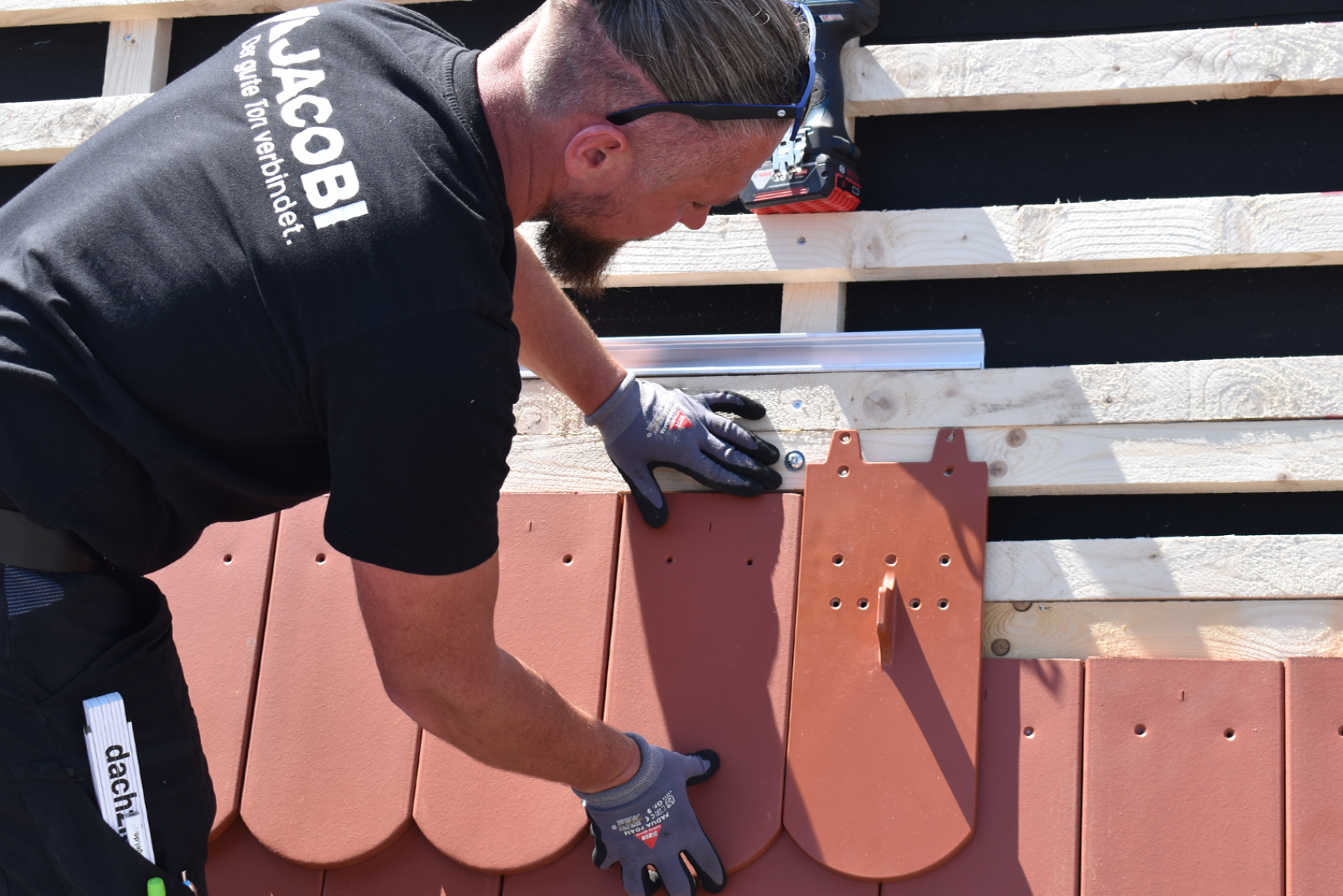 Mitarbeiter deckt Biber-Solarträger in einer Biberschwanzziegel-Dachfläche ein
