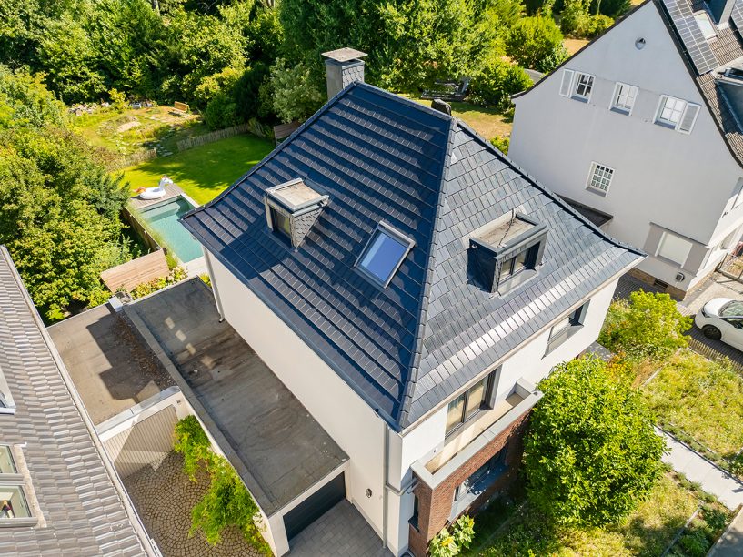 Saniertes Walmdach mit Solarziegel Stylist-PV verleiht Sanierungsobjekt neuen Glanz mit der Drohne von schräg oben fotografiert