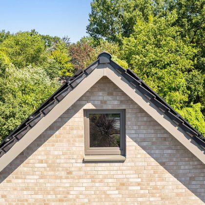 Reformziegel Z12v in samtschwarz auf hellem Backsteinhaus mit Satteldach. Bildfokus Anfangsscheibe am First